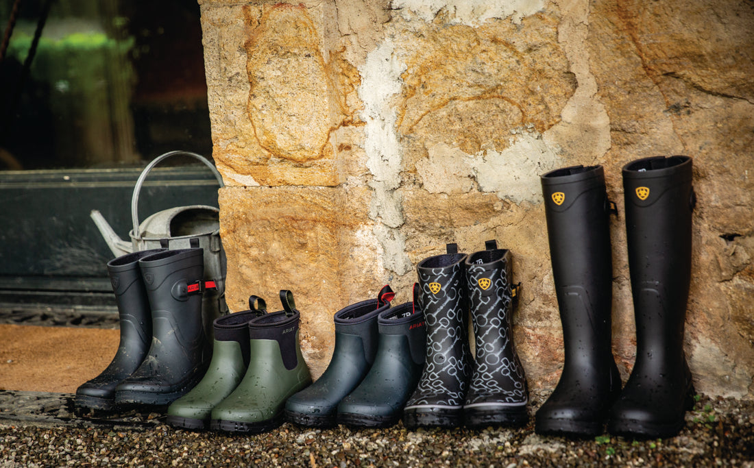 5 pairs of rubber rain boots of varying heights lined against a rock wall